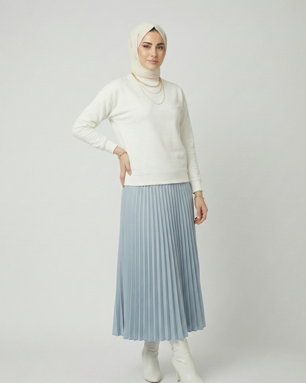 Person wearing a white sweater, light blue pleated skirt, and white boots on a plain background