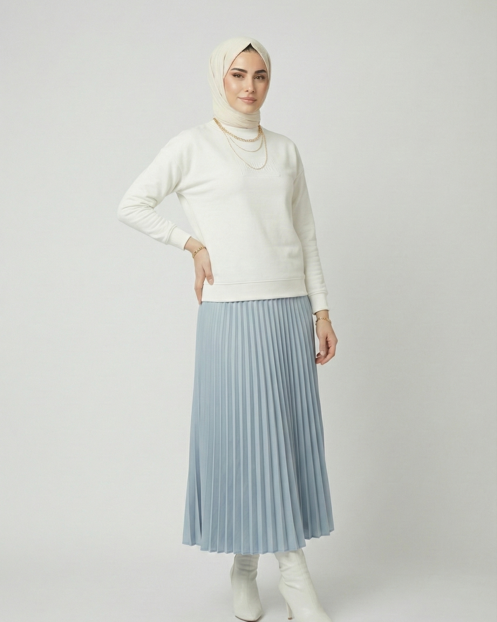 Person wearing a white sweater, light blue pleated skirt, and white boots on a plain background