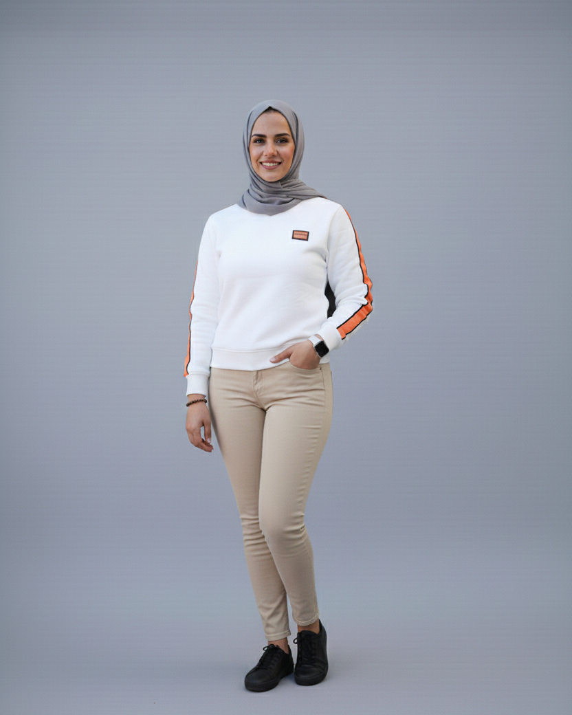 Person wearing a white sweater with orange accents and beige pants on a gray background