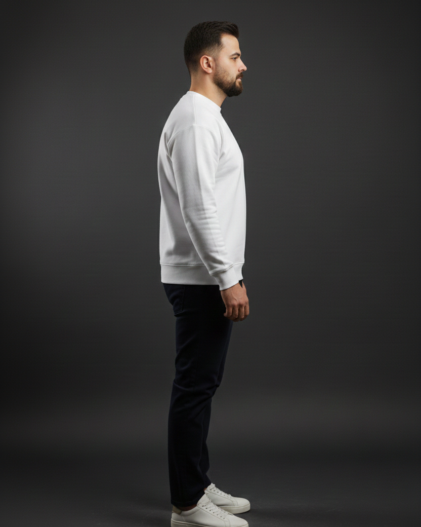 Man wearing a light gray sweater and dark pants standing against a black background