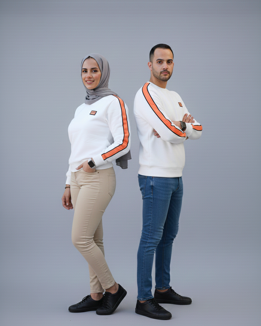 Two people wearing matching white sweaters with orange accents on a gray background